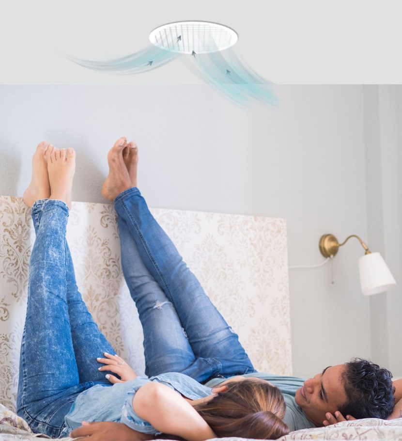 A couple laying on a bed with a whole house fan blowing on them
